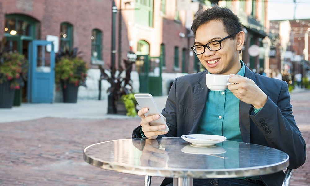 Un homme prend un café tout en consultant son relevé sur son téléphone intelligent.